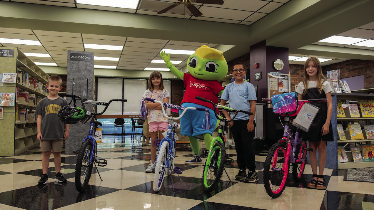 From left: Dak Douglas, Samantha Russo, Special guest Buddy Bookworm, Easton Lemaster, and Allison Tanner — the four winners stand next to the bikes they were rewarded after they completed the Summer Reading Program with a total of 20 books read.