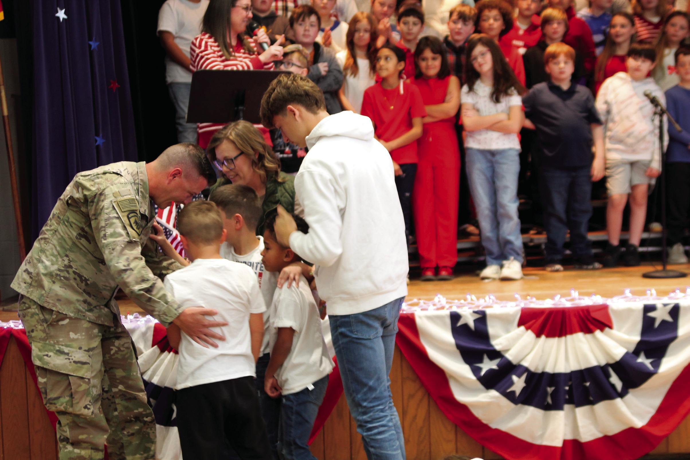 The Quinnelly family have an emotional embrace after Ryan’s surprise return home after a nine month deployment during a Pratt Elementary Veteran’s Day assembly. Photo by DeAnna Maddox