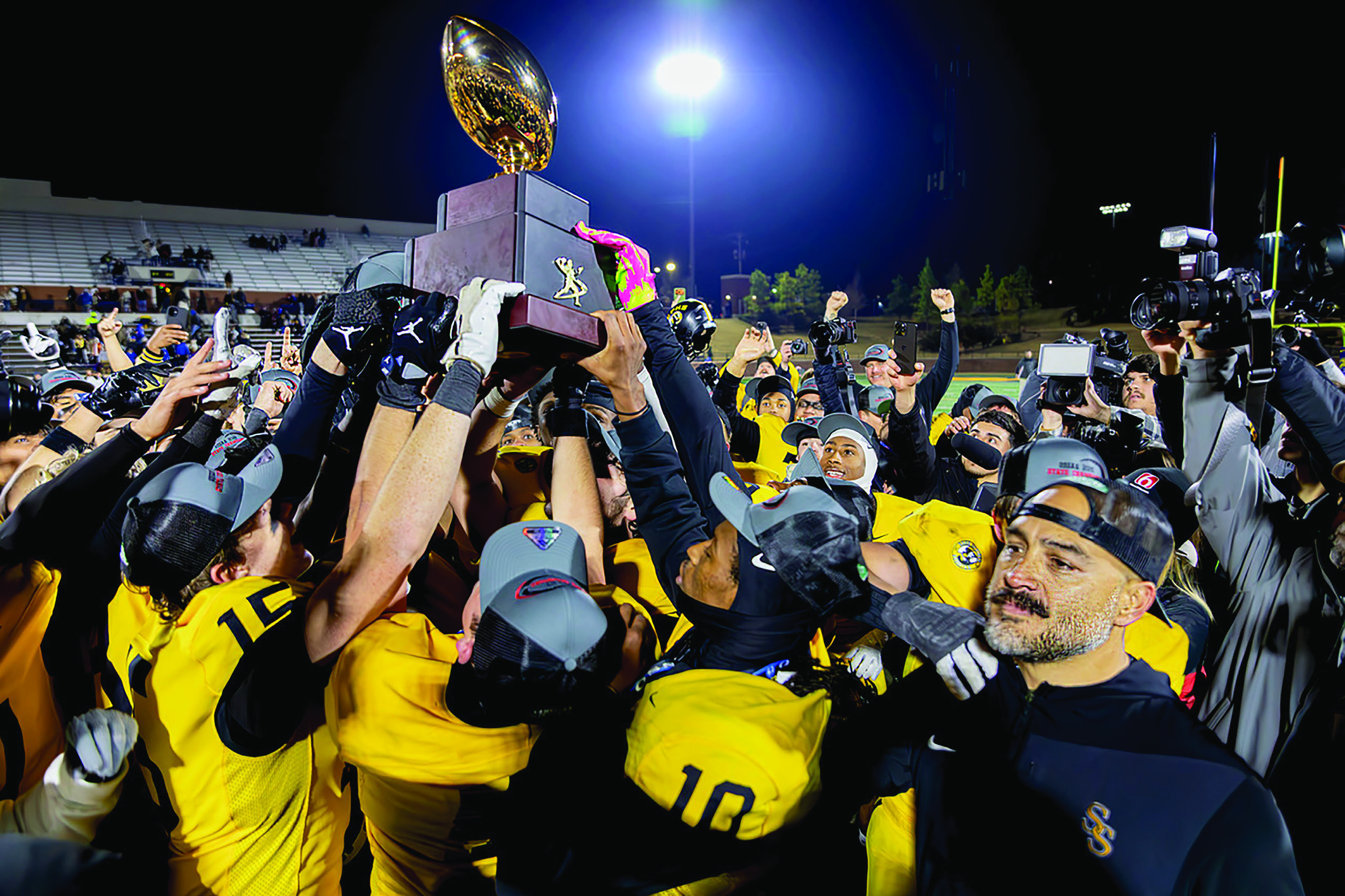 Sandite hands rise together, hoisting the gold ball in celebration as an emotional coach Bobby Klinck leans into the moment and reflects on a shared, hard-fought season that ended in triumph, erased 59 years of waiting and bound a town to its team and a team to its coach. Photo by John Burns