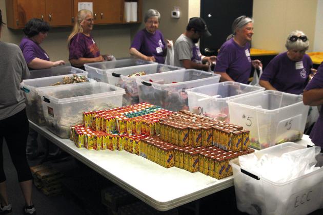 Mannford Food for Kids Backpack Program’s regular volunteers fall into line immediately as they make their way around a table grabbing each item to fill bag after bag of supplementary food for students. Photo by DeAnna Maddox